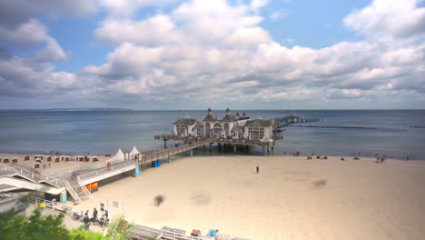 Tourists-Visiting-Sellin-Pier-and-Walking-on-Soft-White-Sandy-Beach-on-Ruegen-Island-in-the-Baltic-Sea-Coast,-Germany---Timelapse-Wide-Angle-Elevated-View