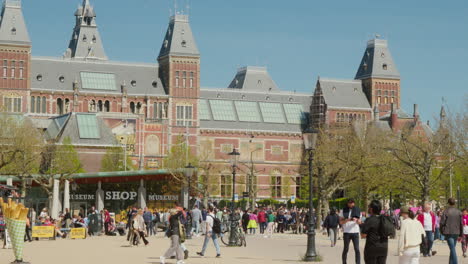Lebendiger-Rijksmuseum-Platz:-Touristen-Gehen-Vor-Dem-Wunderschönen-Historischen-Museum-In-Amsterdam,-Niederlande,-Spazieren,-In-Sonnenlicht-Getaucht