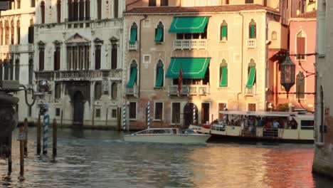 Venetian-boats-full-of-tourist-passing-by-in-the-distance-through-a-water-canal-in-Venice,-Italy