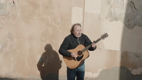 Street-musician-playing-guitar-against-aged-wall-in-Prague,-Czech-Republic