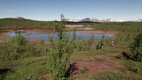 Super-Wide-Aerial-Shot-of-Three-Hikers-walking-on-the-Kungsleden-Trail-in-a-Stunning-Swedish-Mountain-and-Tundra-Landscape,-Lapland,-Tsielekjåkk,-Sunny-Day