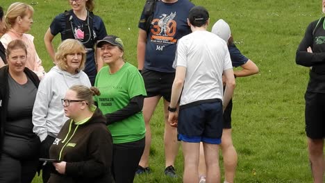 Group-of-runners-gathered-having-a-chat-and-supporting-each-other-in-local-park-field-at-start-of-their-fitness-run