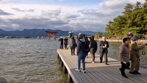 Visitors-on-a-wodden-pier-taking-photos-of-the-famous-floating-torii-of-itsukushima,-Miyajima,-Japan