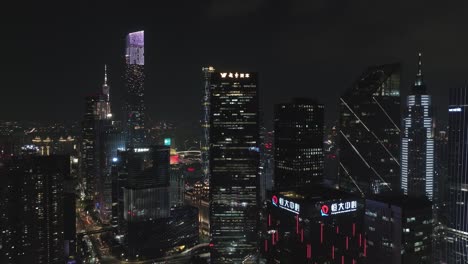Fly-over-Guangzhou-beautifully-illuminated-Central-office-building-district-with-Canton-tower-in-the-distance,-at-night