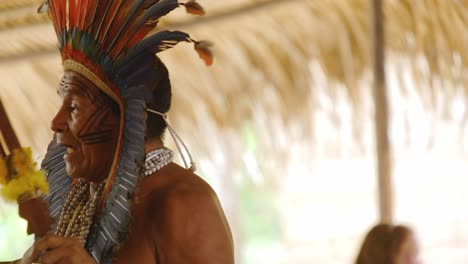 Retrato-De-Primer-Plano-De-Un-Chamán-Amazónico-Espiritual-Con-Tocado-De-Plumas-Hablando-Y-Brindando-Una-Ceremonia-Ritual-De-Medicina-Tradicional,-Brasil