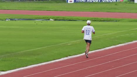 A-man-seen-running-on-a-track-with-a-number-eleven-white-shirt-and-a-cap-while-looking-into-his-time-piece