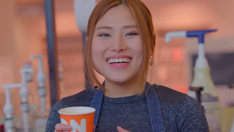 Asian-pretty-girl-gesturing-and-smelling-Dunkin-coffee-out-of-a-cup-and-smiles