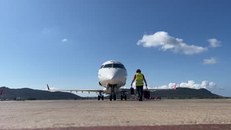 Agente-De-Rampa-Asegurando-Un-Jet-Blanco-De-Tamaño-Mediano-Con-Calzos-En-El-Aeropuerto-De-Ibiza-Justo-Después-De-La-Llegada-Del-Avión.
