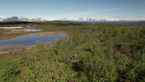 Super-Wide-Aerial-Shot-of-Three-Hikers-walking-on-the-Kungsleden-Trail-in-a-Stunning-Swedish-Mountain-and-Tundra-Landscape,-Lapland,-Tsielekjåkk,-Sunny-Day