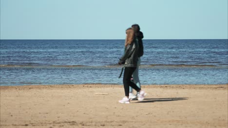 Jurmala-beach-soft-waves,-Latvia,-with-a-couple-of-girls-passing-by
