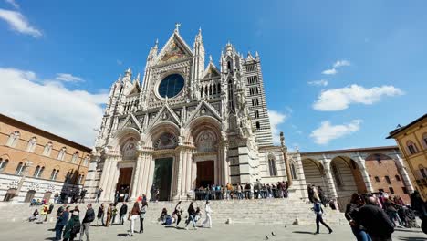 Group-of-people-walking-in-front-and-lining-up-to-visit-the-Siena-Cathedral-,-Tuscany-region,-Siena,-Italy-on-a-sunny-day
