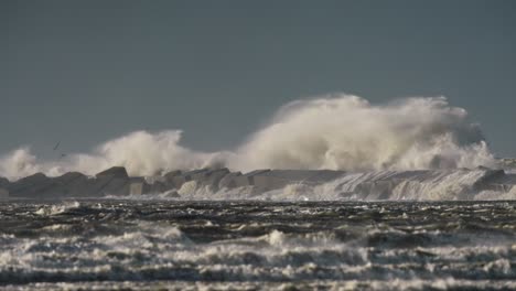 Wide-shot-of-giant-waves-crashing-over-the-breakwater-and-sending-up-spray-during-an-extreme-storm,-slow-motion