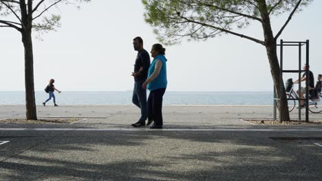 Menschen,-Die-An-Der-Strandpromenade-Von-Thessaloniki-Vorbeikommen,-Meereshintergrund,-Sonniger-Tag,-Sommer