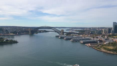 Atemberaubende-Rückluftaufnahmen-Des-Hafens-Von-Sydney-Zeigen-Das-Berühmte-Opernhaus-Von-Sydney,-Die-Majestätische-Sydney-Harbour-Bridge-Und-Die-Fähre-Auf-Glitzerndem-Wasser