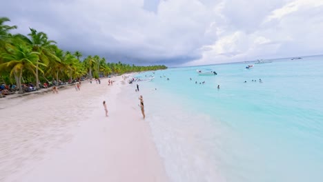 People-bathing-and-relaxing-in-turquoise-water-of-Saona-Island-sea-on-cloudy-day,-Dominican-Republic