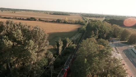 Captivating-aerial-drone-footage-follows-a-laden-cargo-tank-train-passing-through-vast-golden-lit-cornfields,-as-the-drone-soars-above,-revealing-the-stunning-rural-scenery