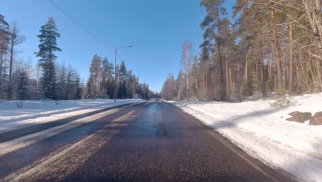 The-car-smoothly-travels-along-the-snow-covered-road,-flanked-by-towering-pines,-creating-a-captivating-winter-tableau-that-showcases-the-harmonious-blend-of-nature-and-mobility