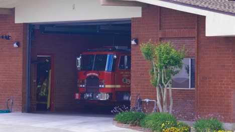Static-real-time-shot-of-a-Los-Angeles-County-fire-station-with-a-firetruck-ready-for-action-and-firefighters'-turnout-gear-showing-in-the-firehouse