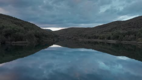 Fast-Drone-over-calm-mountain-lake-waters-reflecting-sunset-colour-clouds