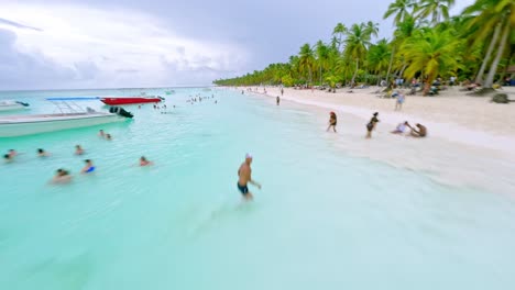 People-on-beach-and-bathing-in-turquoise-water-of-Saona-Island-sea,-Dominican-Republic