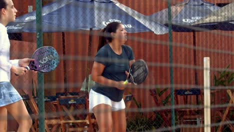 View-through-court-fence-of-two-girls-playing-beach-tennis-in-slow-motion-in-Brasilia,-Brazil