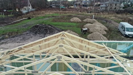 Timber-frame-truss-roof-system-at-a-home-construction-site---pullback-aerial-reveal