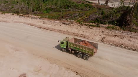 Green-dump-truck-drive-on-dusty-road-and-carry-gravel-near-felled-forest