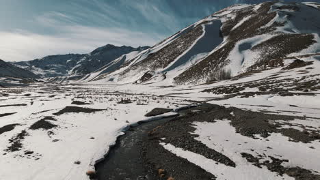 Drone-speeding-over-a-river-in-a-snowy-Andean-valley,-capturing-the-breathtaking-beauty-of-the-mountainous-landscape