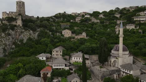 Vista-De-Drones-De-La-Histórica-Ciudad-Bosnia-Construida-A-Orillas-Del-Río-Neretva,-El-Castillo-De-La-Popular-Ciudad-Bosnia-De-Pocitelj-Con-Sus-Edificios-De-Piedra-Y-Su-Paisaje-Verde