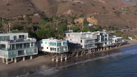 Aerial-pullback-of-beachfront-home-over-the-Pacific-Ocean-in-Malibu,-establishing-shot