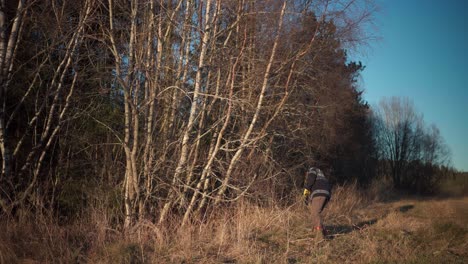 Man-Holding-Small-Chainsaw-As-He-Walks-On-Rural-Landscape-To-Cut-Down-Trees