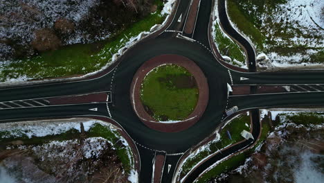 Drop-down-view-roundabout-intersection-in-cold-winter-weather-with-light-traffic-and-snow