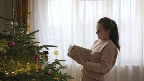 Ein-Mädchen,-Das-Neben-Dem-Weihnachtsbaum-Steht,-Wirft-Ein-Geschenk-In-Die-Luft-–-Mittlere-Nahaufnahme