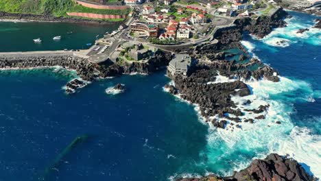 Panoramic-aerial-pullback-reveals-Porto-Moniz-natural-pools-of-vibrant-blue-ocean-water-and-terraced-city,-Madeira-Portugal