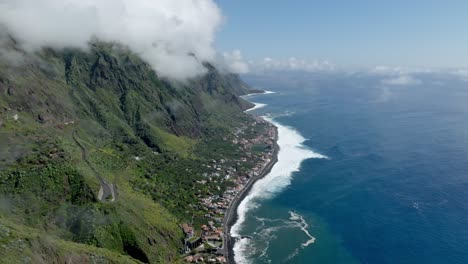 Aerial-trucking-pan-reveals-clouds-gathered-on-mountain-top-above-coastal-town-in-Madeira-Portugal