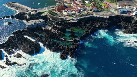Ocean-waves-crash-against-jagged-rocky-basalt-in-Porto-Moniz-natural-pools,-aerial