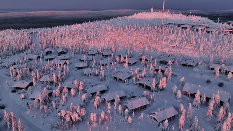 Drone-circling-snowy-cottages-on-the-Iso-Syote-fjell-summit,-sunrise-in-Finland