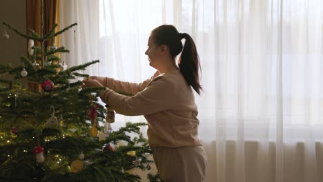 Una-Niña-Está-Ajustando-Las-Decoraciones-Colgantes-En-El-árbol-De-Navidad---Primer-Plano-Medio