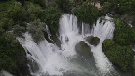 View-from-above-of-water-flowing-through-trees-at-the-Kravica-waterfall-in-Bosnia,-the-image-created-by-the-rapid-flow-of-water
