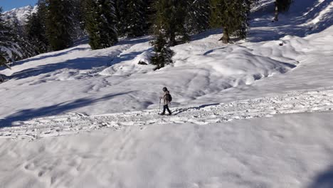 Aerial-tracking-shot-of-woman-snowshoeing-on-snowy-path-downhill-swiss-mountains-at-sunny-day---orbiting-shot