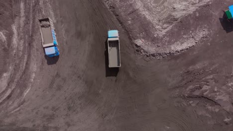 Aerial-top-down-view-of-dump-trucks-drive-on-dusty-coal-mine-site-road