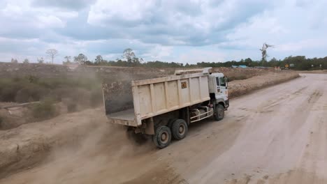 Aerial-follow-of-dump-truck-with-empty-open-box-bed-drive-on-bumpy-dirt-road