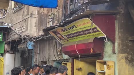 Shot-of-locals-walking-around-busy-narrow-alley-in-Kolkata,-India-with-rows-of-snack-shops