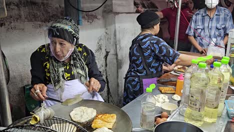 Michelin-awarded-street-food-restaurant,-old-lady-flipping-food-in-hot-pan