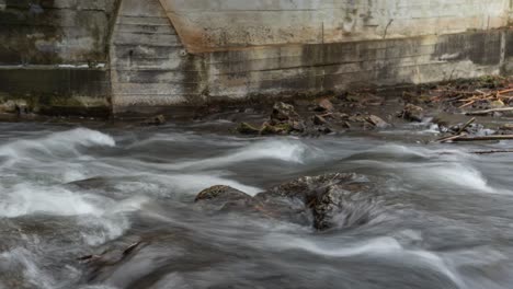 Timelapse-of-river-current-flowing-over-rocks-along-concrete-dam-wall