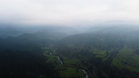 Cinematic-drone-shot-of-river-surrounded-by-green-mountain-landscape-during-foggy-day-in-Nepal,-Asia---Panorama-view