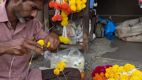 Close-up-view,-a-shopkeeper-is-making-fresh-flower-garlands-on-the-street-road