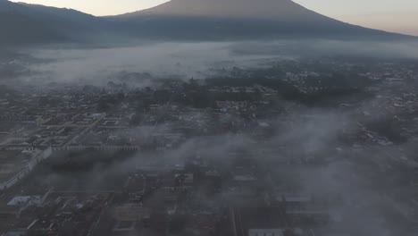 Backwards-flying-at-Antigua-city-Guatemala-during-foggy-morning,-aerial