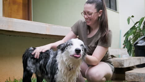Woman-with-glasses-and-her-Australian-Shepherd-dog-enjoying-a-moment-together-in-her-garden,-she-happily-gives-him-a-bath