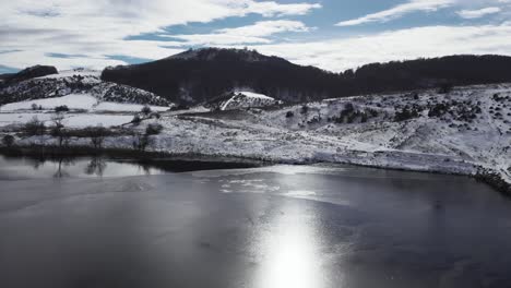 Antena-Lenta-Sobre-Un-Lago-De-Montaña-Cubierto-De-Nieve-Congelado-Soleado-Día-De-Invierno
